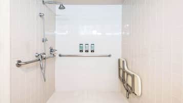 A bathroom with white tiled walls, a shower with a grab bar, and two hand dryers on the wall.