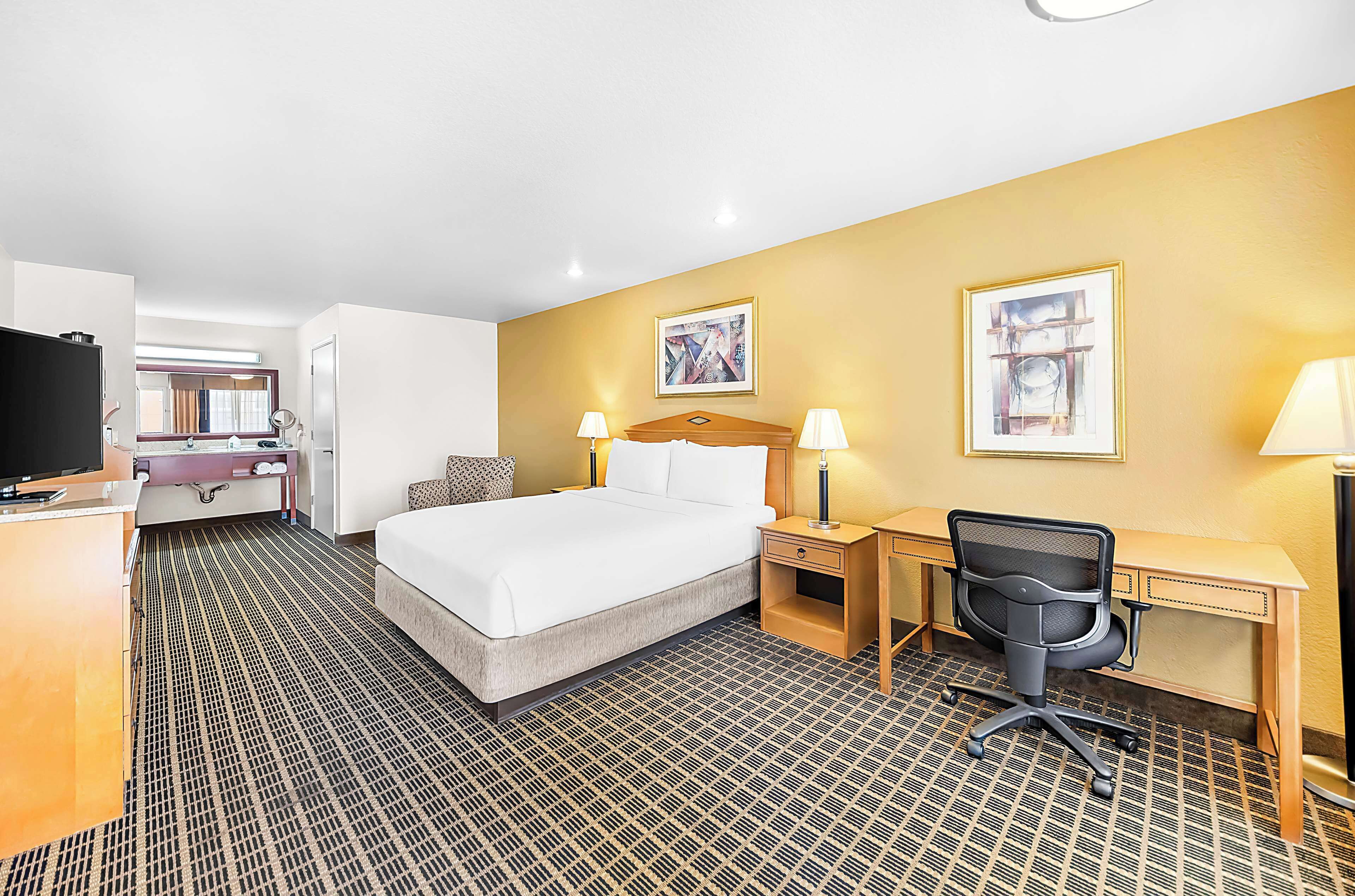 A hotel room with a bed, desk, chair, and a television.