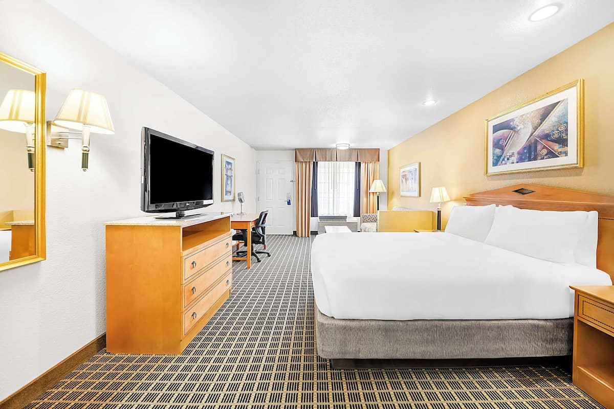 A hotel room with a large bed, a desk with a computer, a television, and a bathroom visible in the background.
