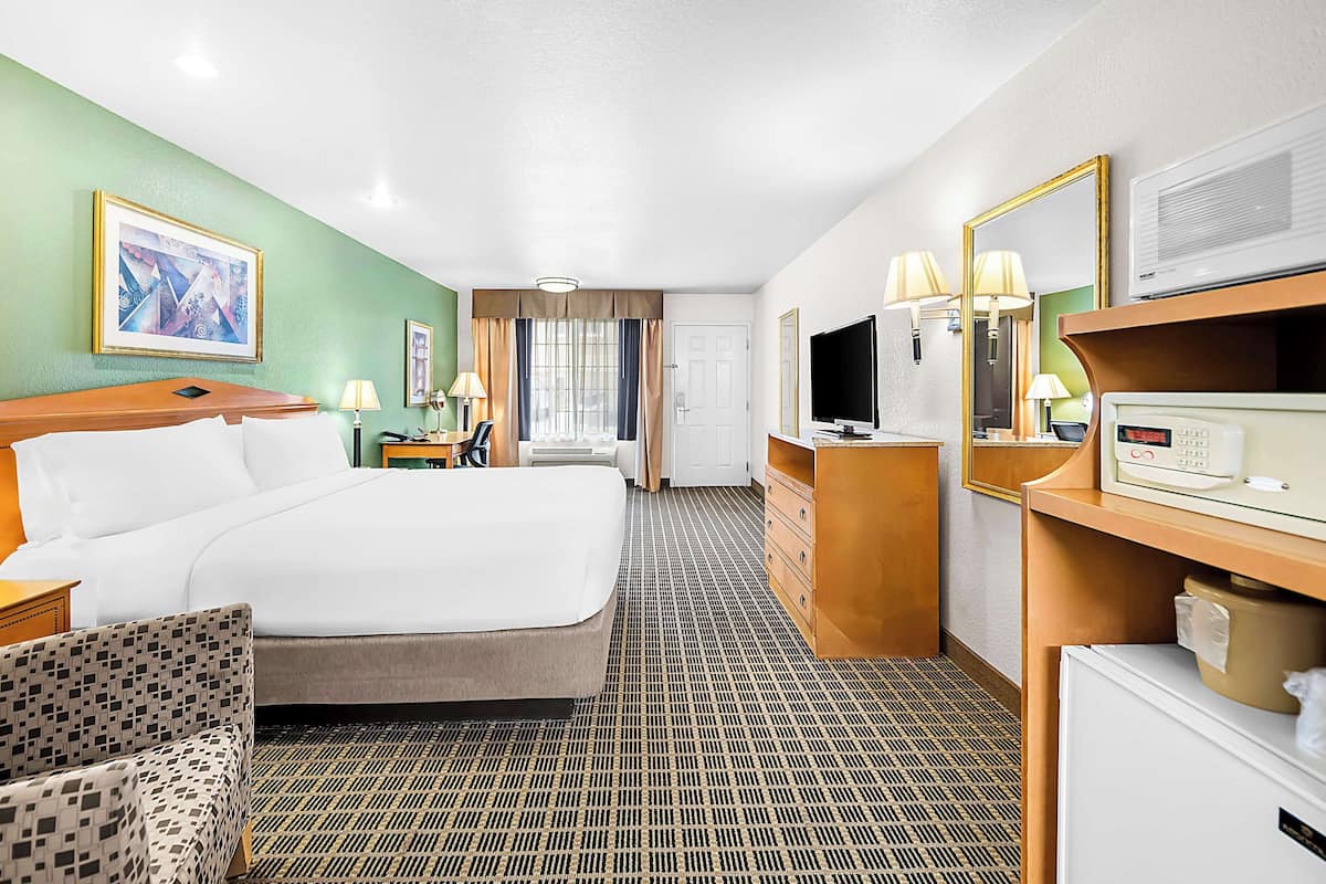 A hotel room with a large bed, a desk with a computer, a television, and a minibar.