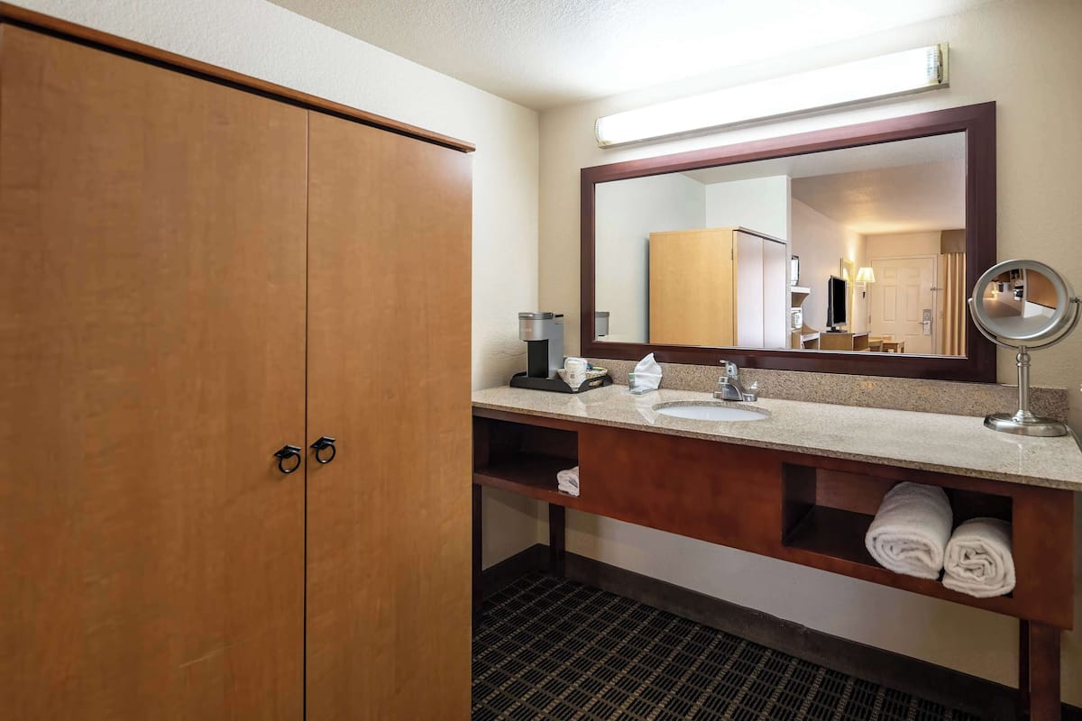 A hotel bathroom with a wooden wardrobe, a sink with a mirror, and a towel rack.