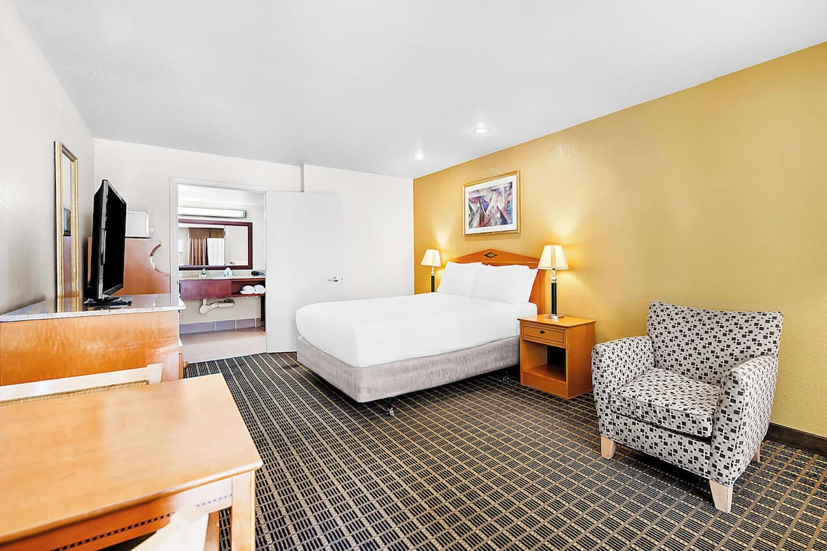A hotel room with a bed, a desk, a chair, and a TV.