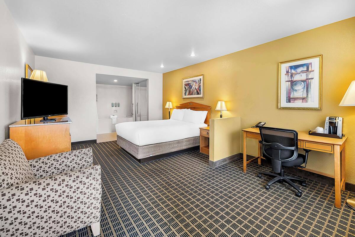 A hotel room with a bed, desk, chair, TV, and two lamps.