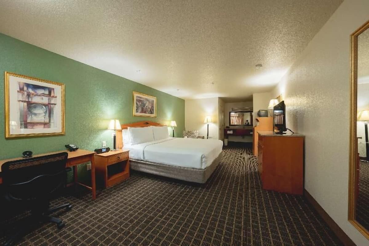 A hotel room with a bed, desk, chair, lamps, and a mirror.