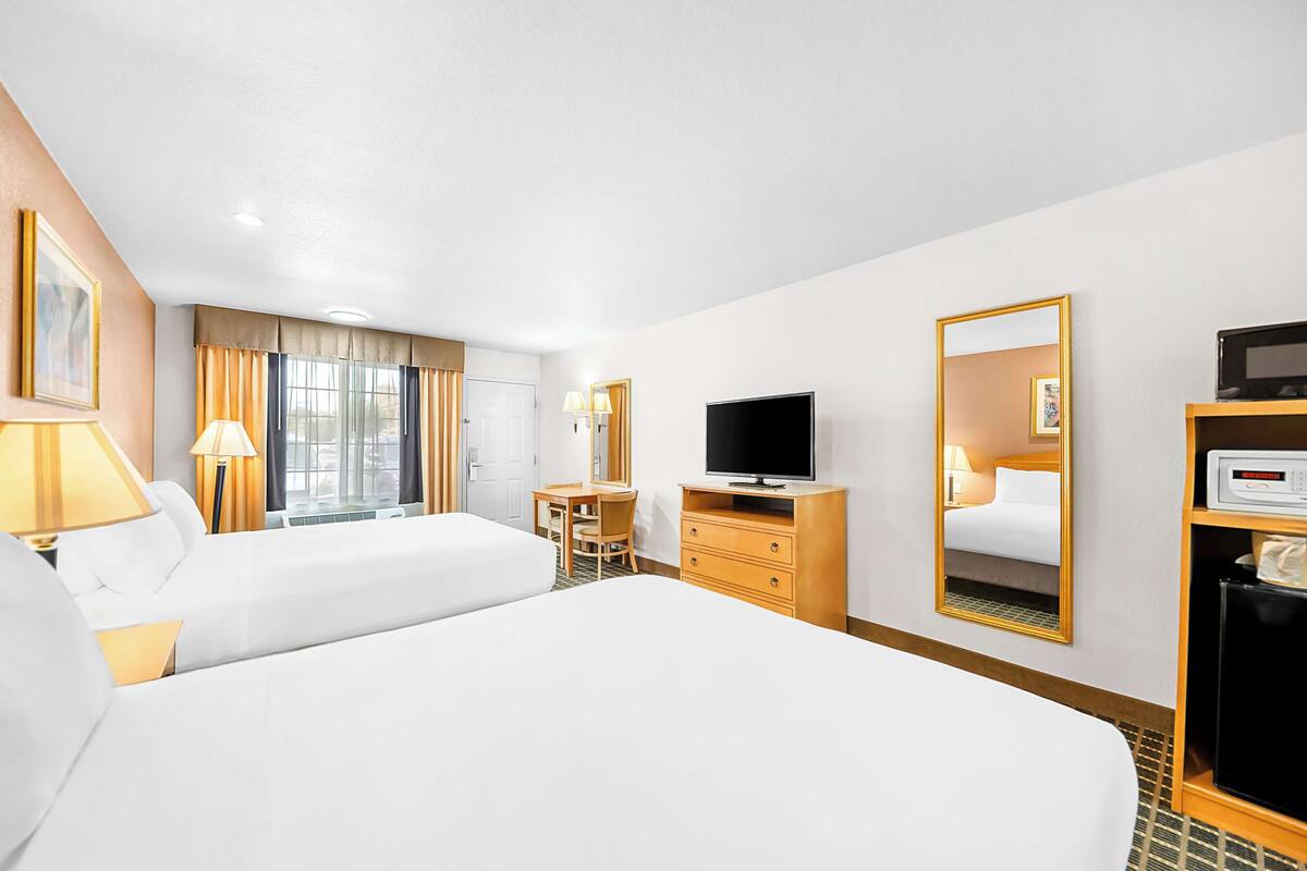 A hotel room with two beds, a desk, a television, a mirror, and a wardrobe.