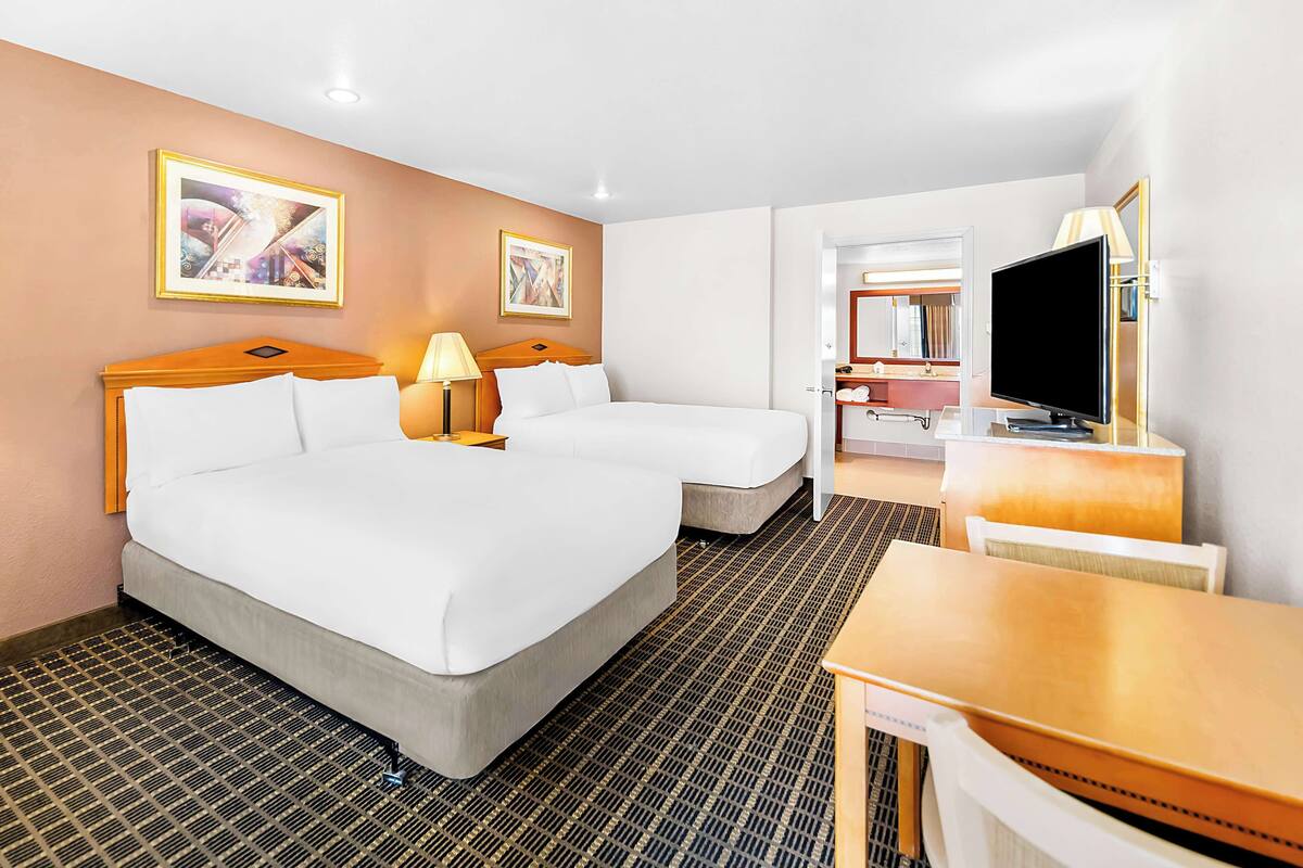 A hotel room with two beds, a desk, a TV, and artwork on the walls.
