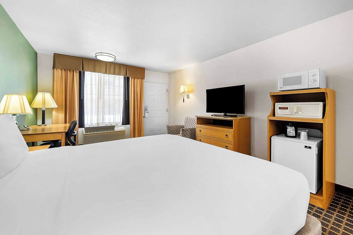A hotel room with a large bed, a desk with a lamp, a television, a microwave, and a mini-fridge.