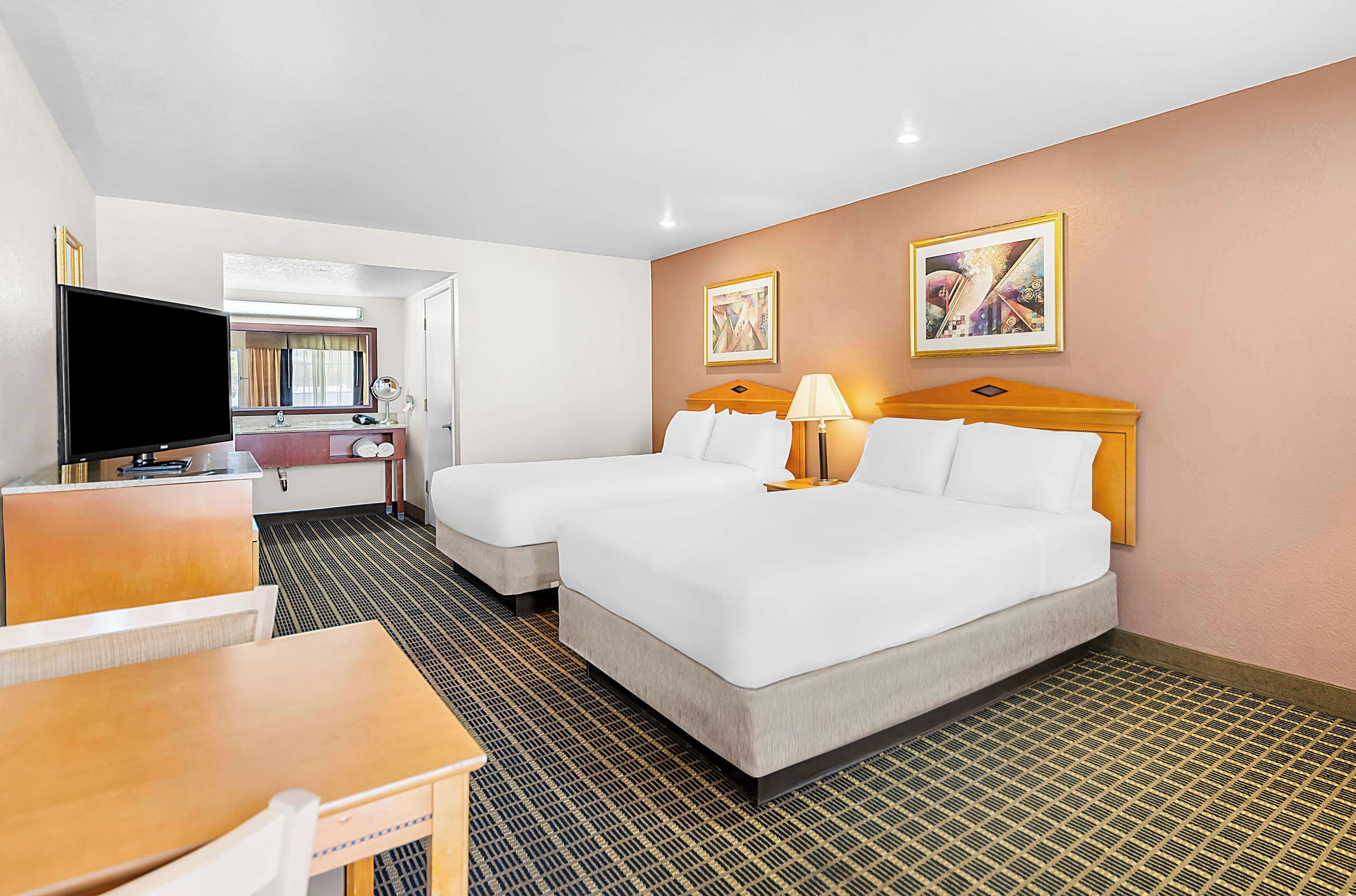 Une chambre d’hôtel avec deux lits, un bureau, une télévision et une salle de bain visible à travers une porte ouverte.