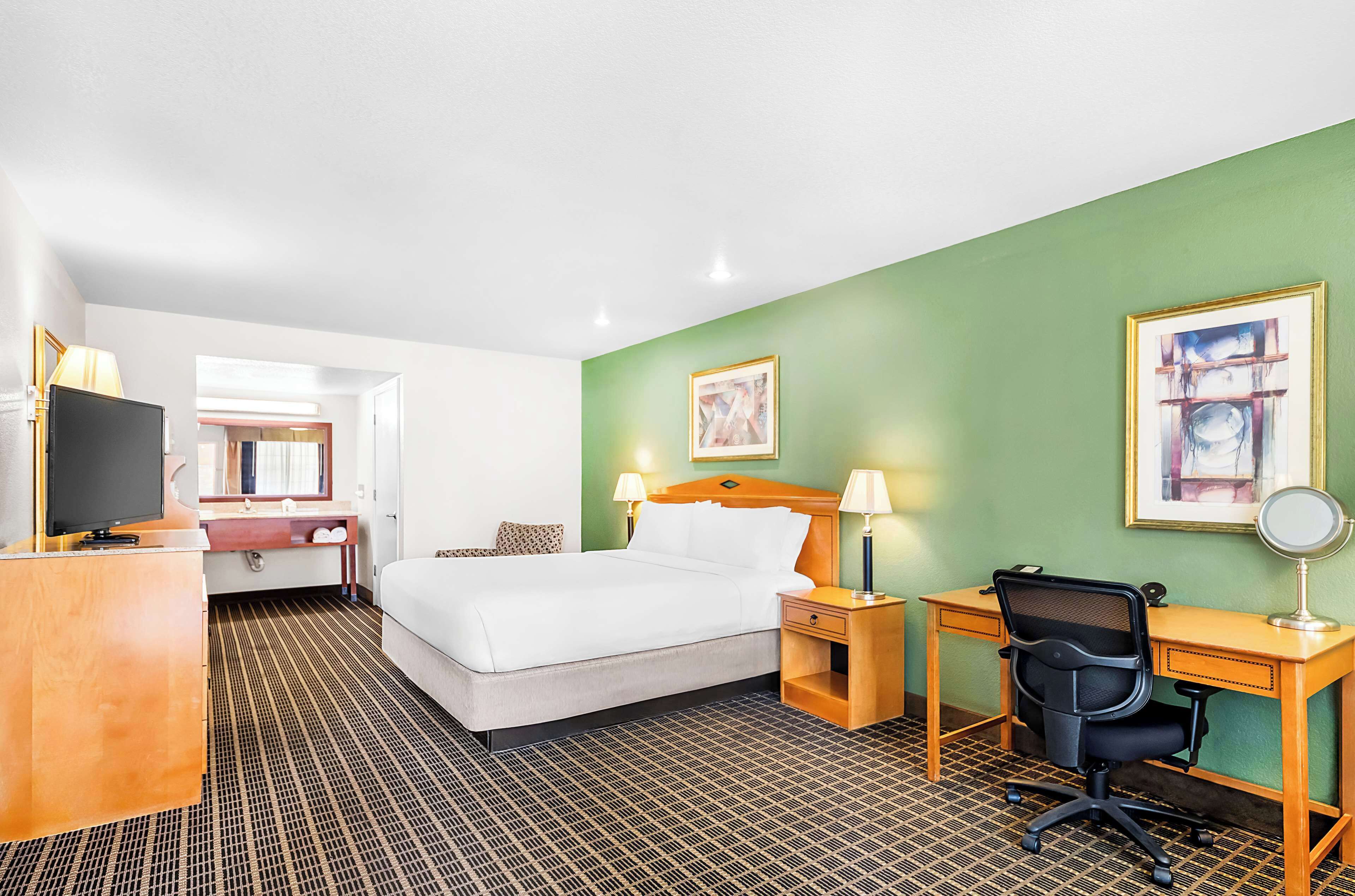 A hotel room with a bed, desk, chair, and a television.