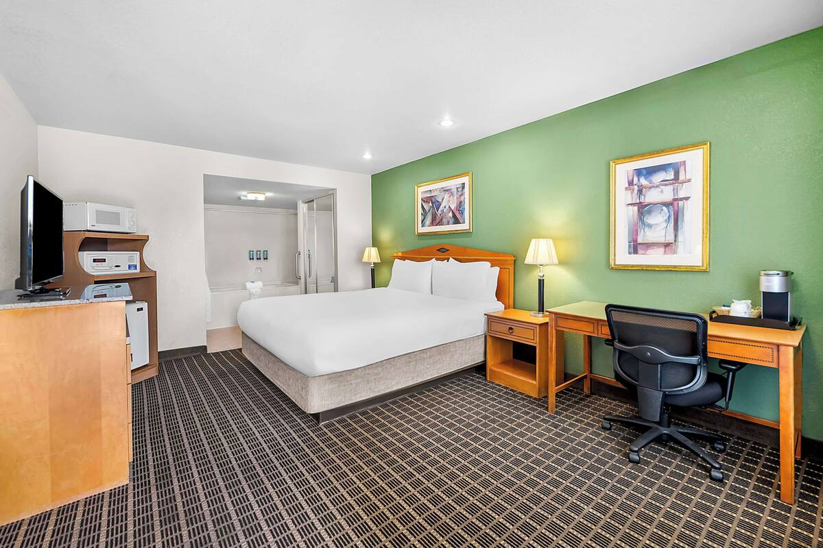 A hotel room with a bed, desk, chair, and a microwave.
