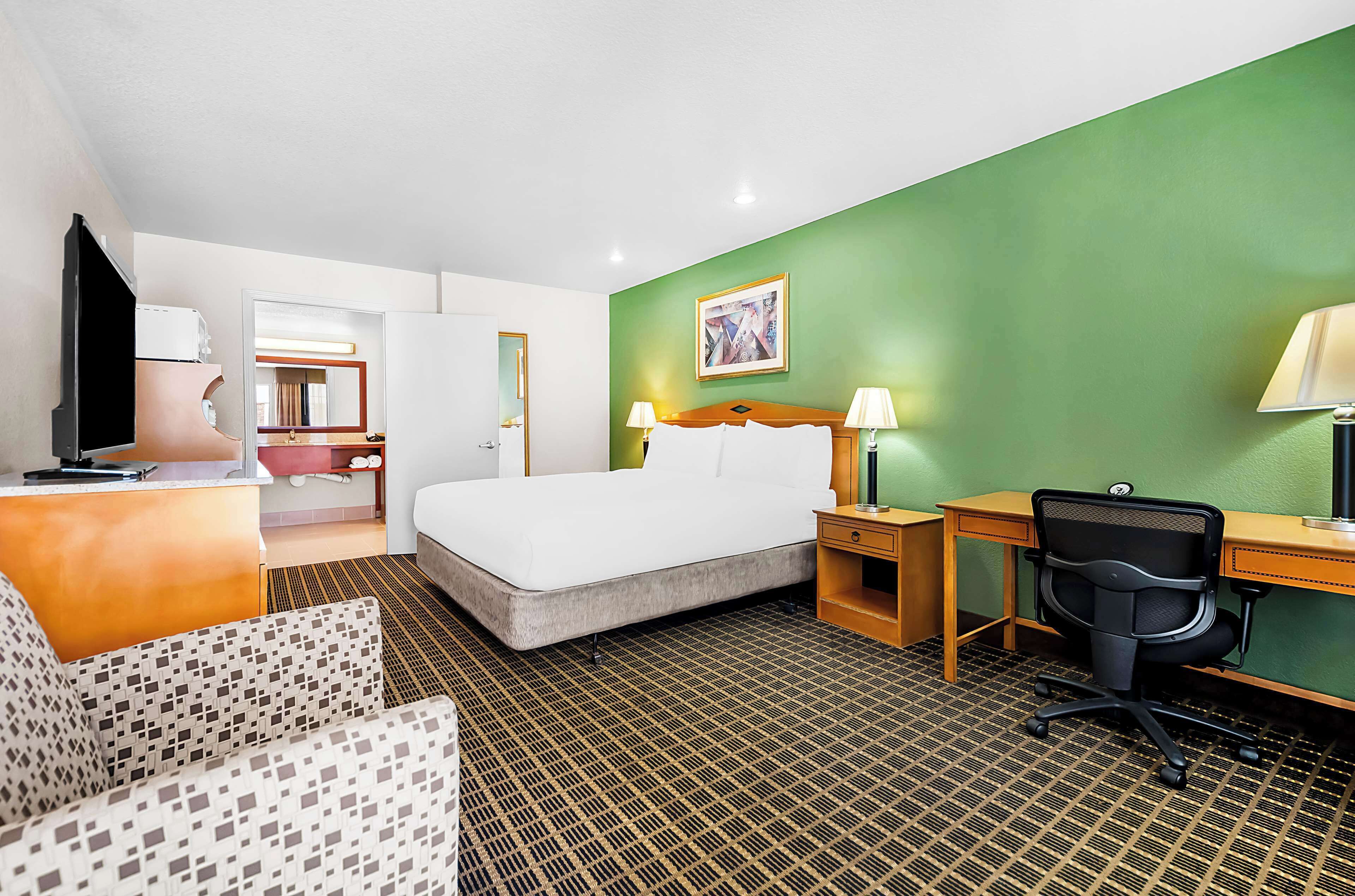A hotel room with a bed, a desk, a chair, a sofa, and a TV.