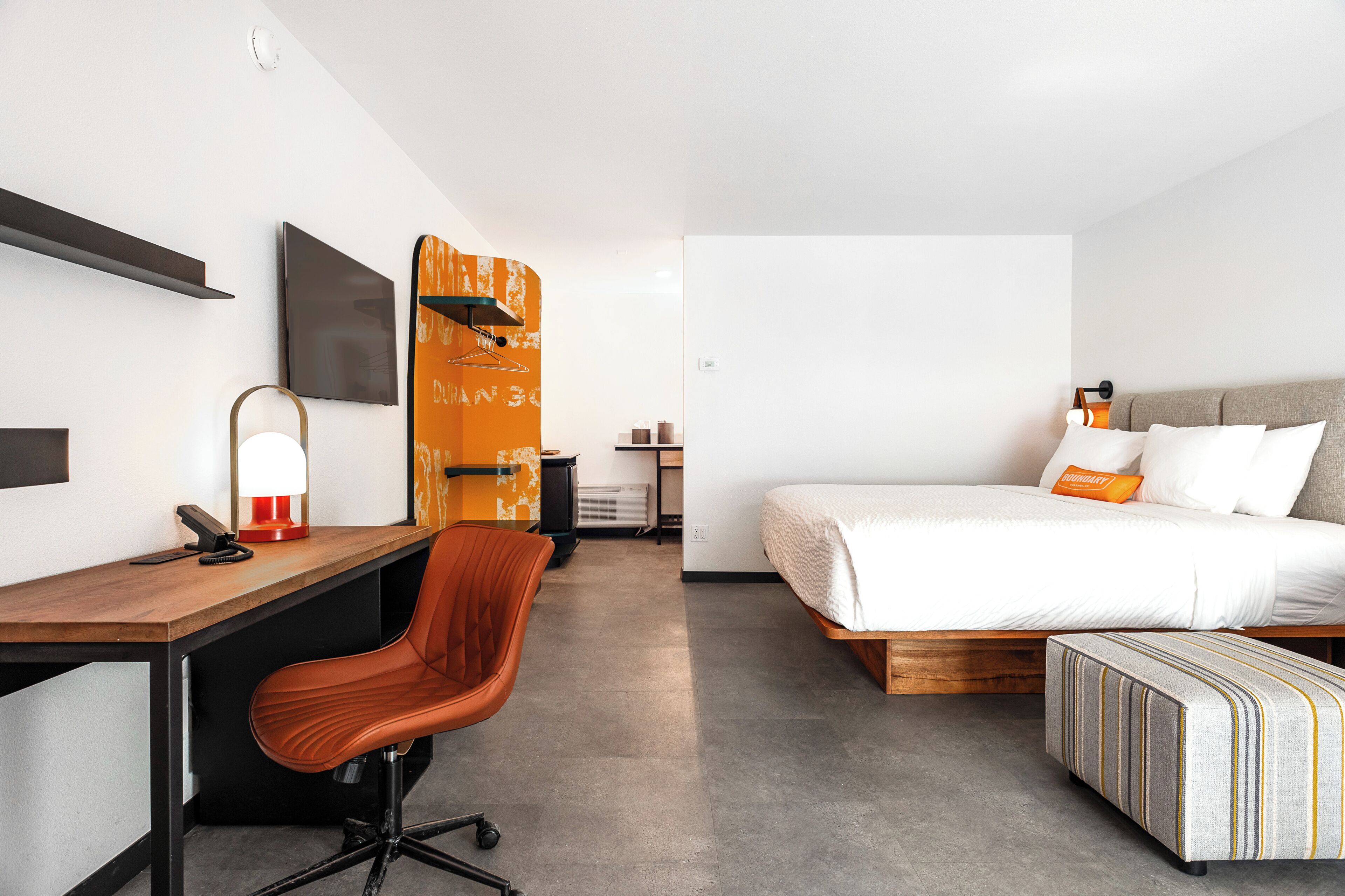 Une chambre d’hôtel moderne équipée d’un bureau, d’une chaise, d’un lit et d’une petite table avec une lampe.