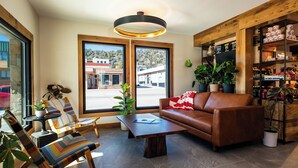 A modern living room with a brown leather sofa, striped chairs, a coffee table, and a wooden bookshelf. - Boundary Hotel By Terra Vi Durango (Durango)