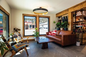 Una sala de estar moderna con un sofá de cuero marrón, sillas a rayas, una mesa de centro y una estantería de madera.