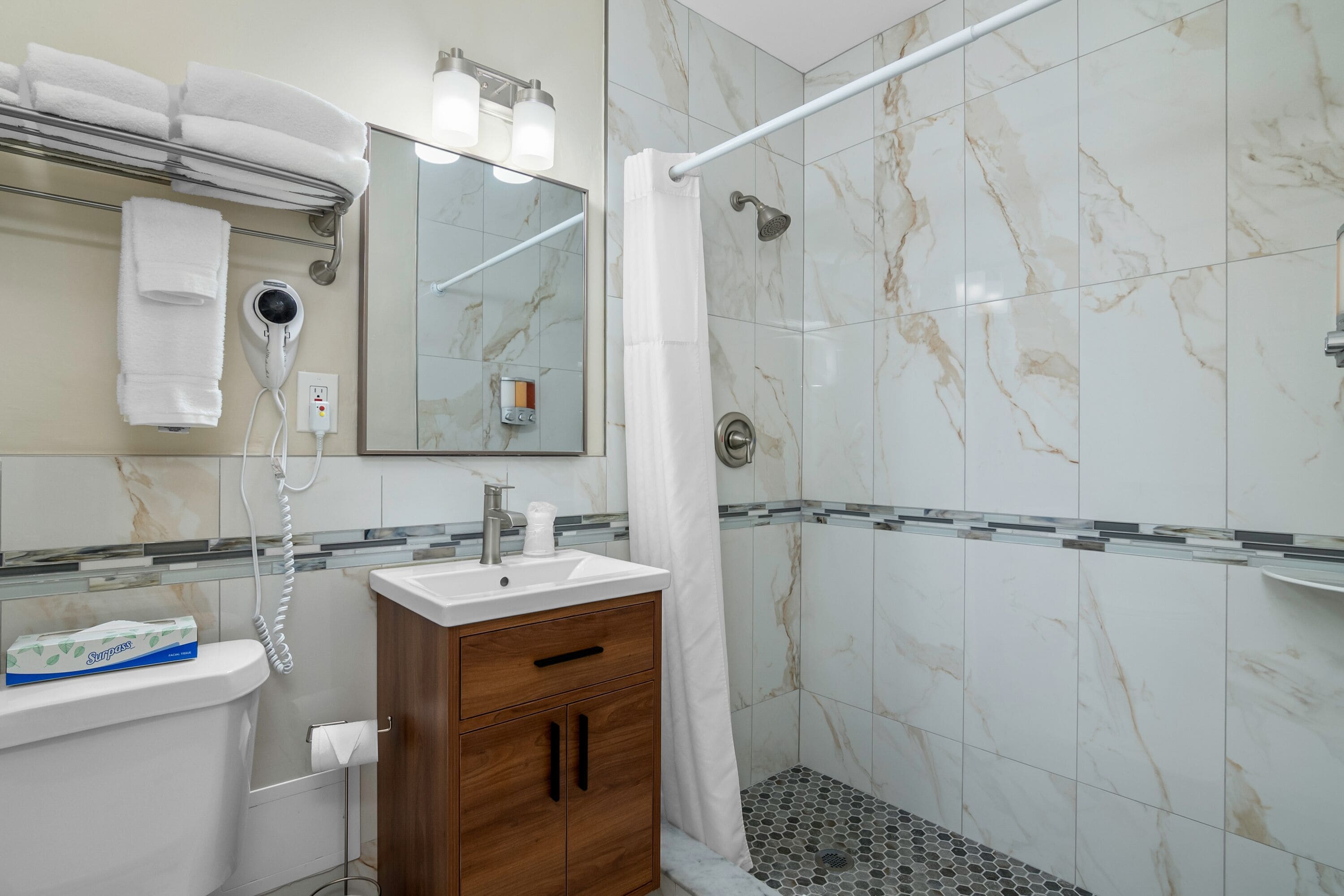 Ein modernes Badezimmer mit einer Marmordusche, einem Waschtisch und einem an der Wand befestigten Föhn.