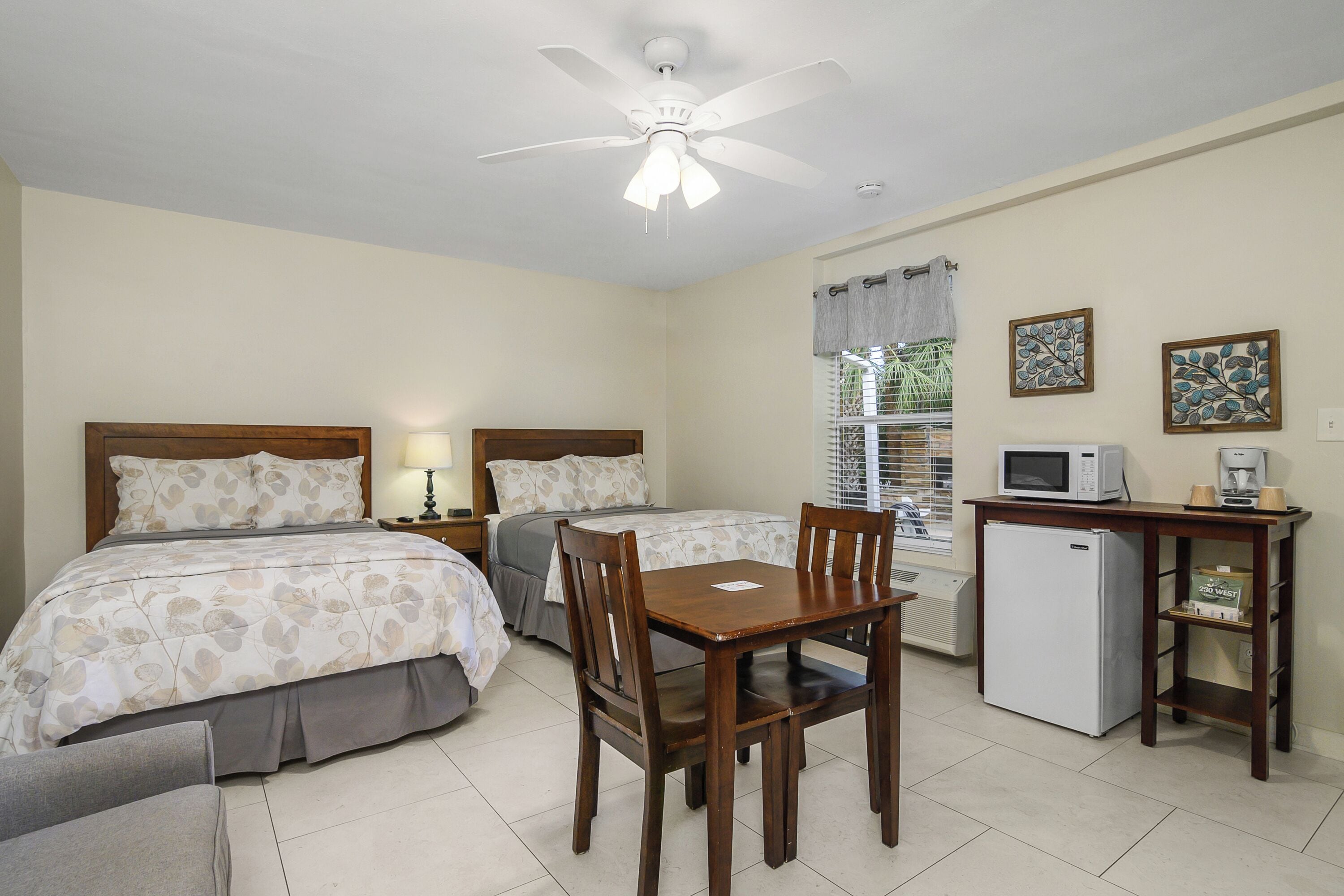 A bedroom with two beds, a desk with a microwave, a refrigerator, and a window with curtains.