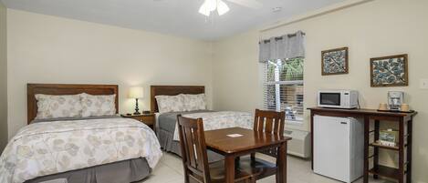 A bedroom with two beds, a desk with a microwave, a refrigerator, and a window with curtains.