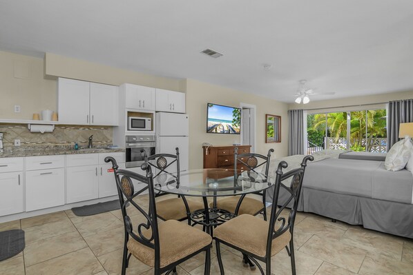 A modern kitchen with white cabinets, a dining table with chairs, a bed with a view, and a ceiling fan.