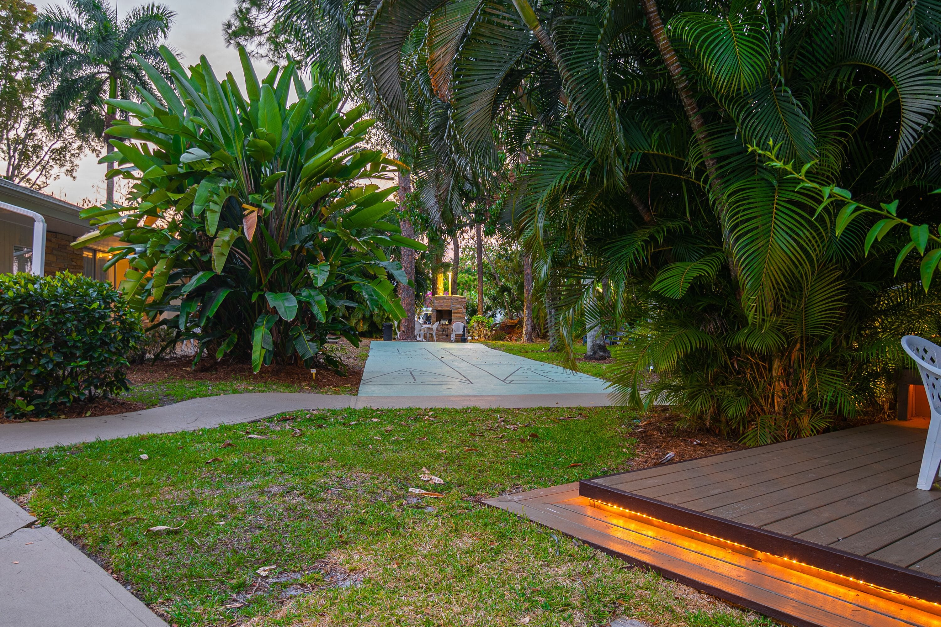 A garden with a wooden deck, a concrete pathway, and various tropical plants.