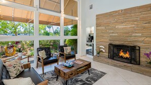 A spacious living area with a stone fireplace, comfortable seating, and large windows offering a view of greenery.