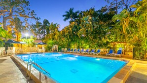A swimming pool with lounge chairs and umbrellas, surrounded by tropical vegetation.