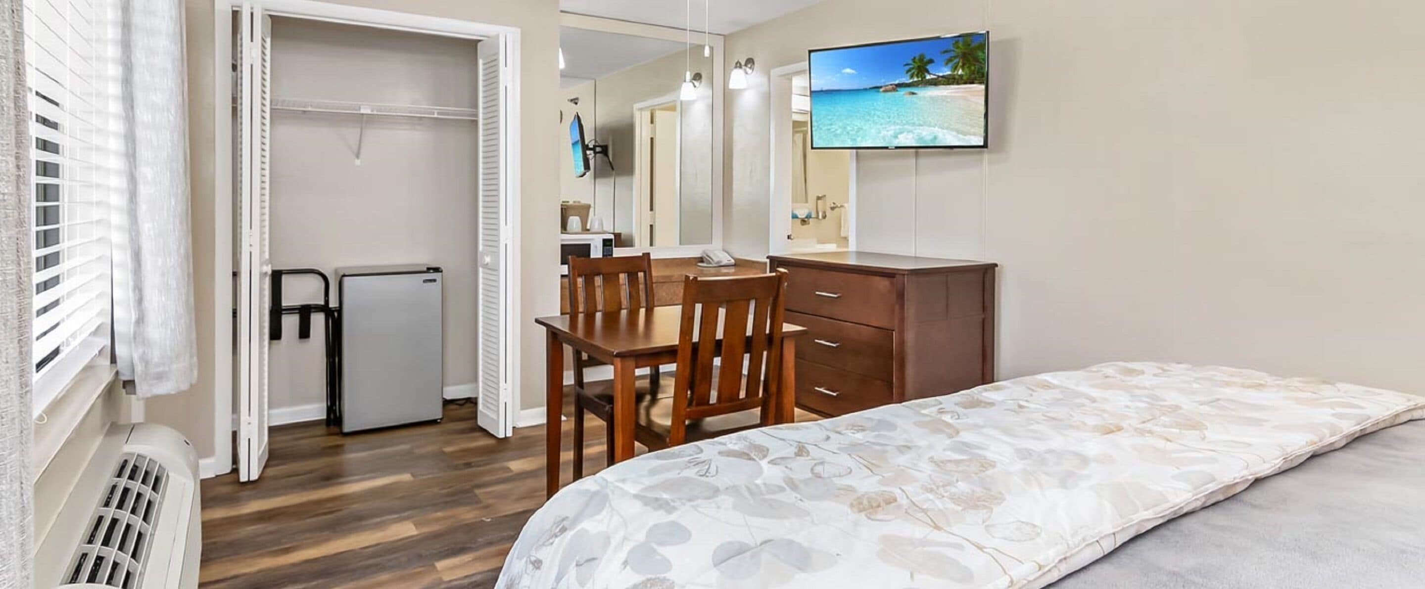 Un dormitorio con una cama, un escritorio, una silla, un aparador y un televisor en la pared.