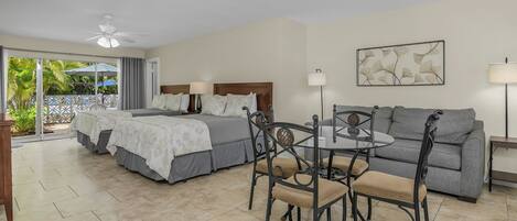 A hotel room with a bed, a sofa, a dining table with chairs, and a ceiling fan.