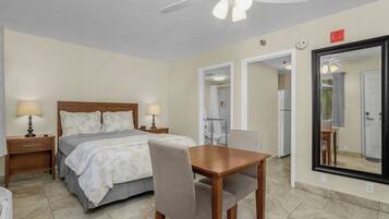 A hotel room with a bed, bedside tables, a desk with a chair, a ceiling fan, and a large mirror.