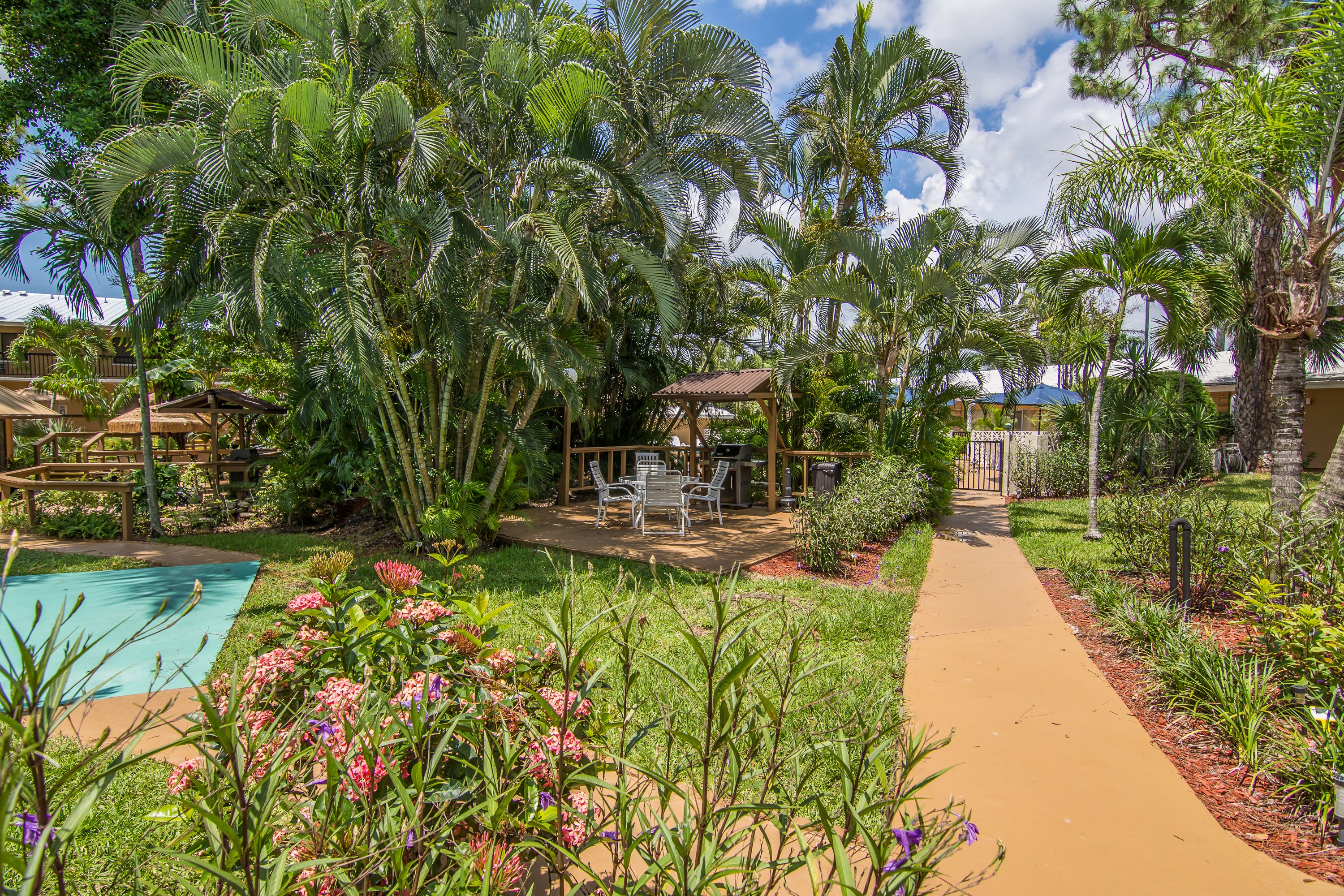 Un giardino tropicale con piscina, un padiglione e un vialetto.