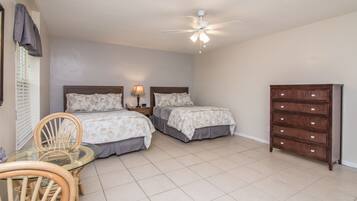 A bedroom with two beds, a wooden dresser, a glass table with a chair, and a ceiling fan.