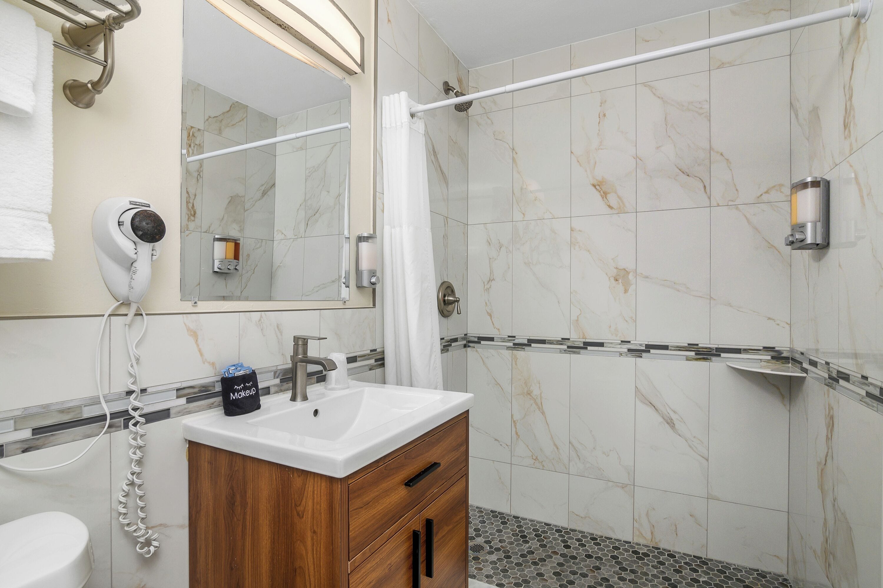 A bathroom with a marble-tiled shower, a white sink, and a wooden vanity.