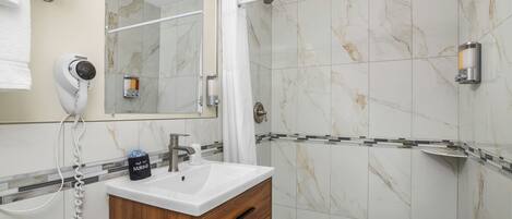 A bathroom with a marble-tiled shower, a white sink, and a wooden vanity.