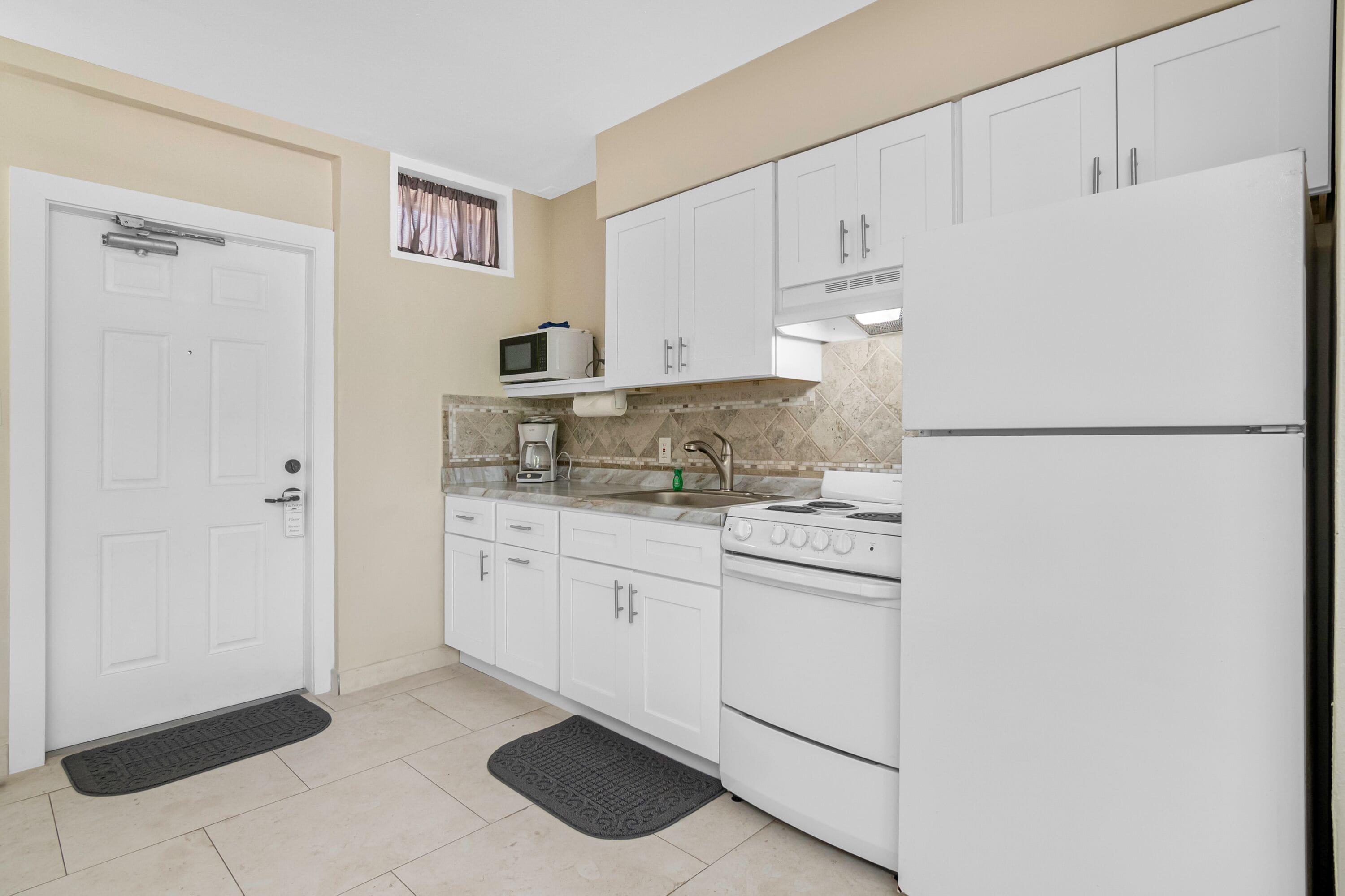 Una cocina compacta con armarios blancos, microondas, estufa y refrigerador.