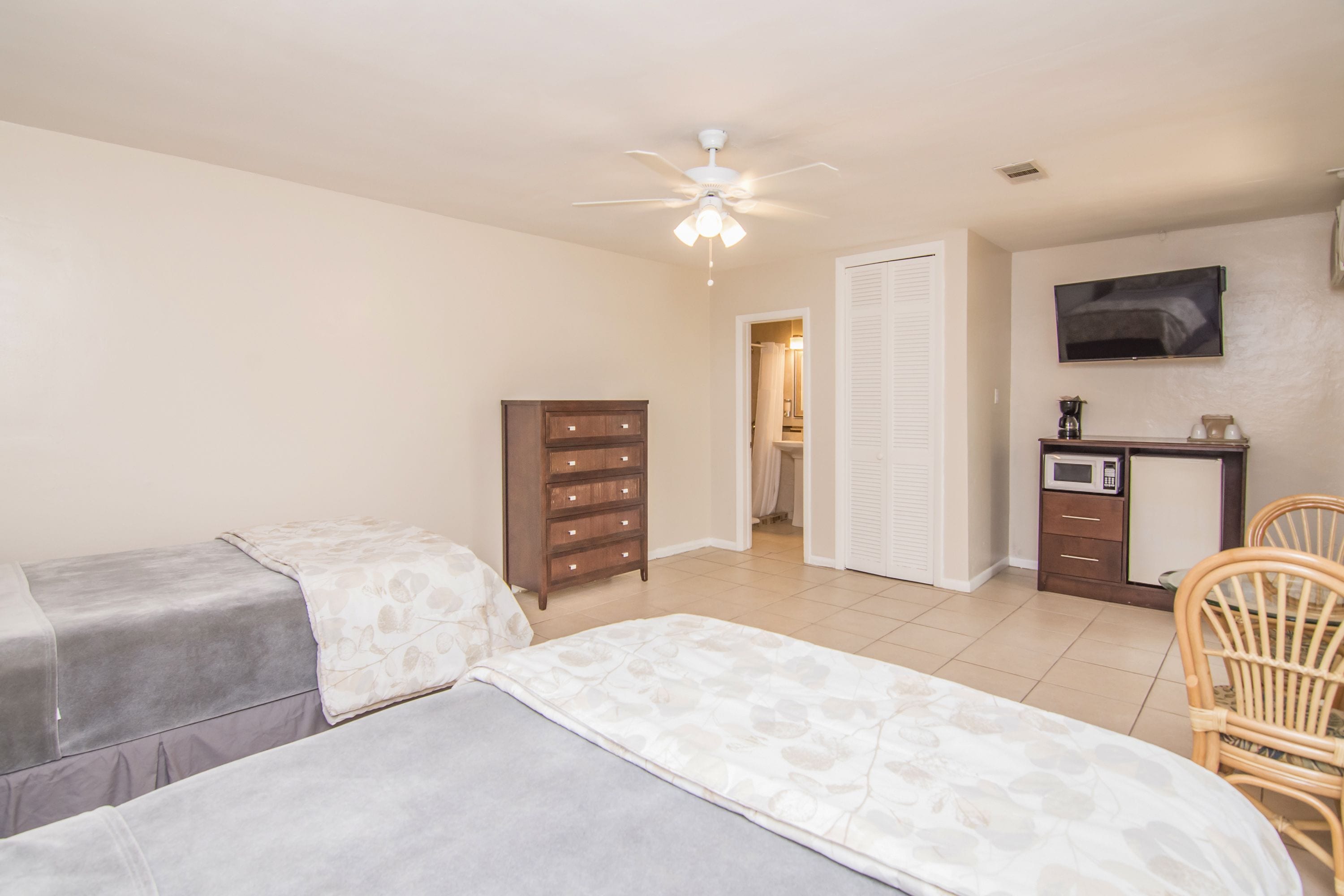 A bedroom with two beds, a ceiling fan, a TV, a desk with a microwave, and a chair.