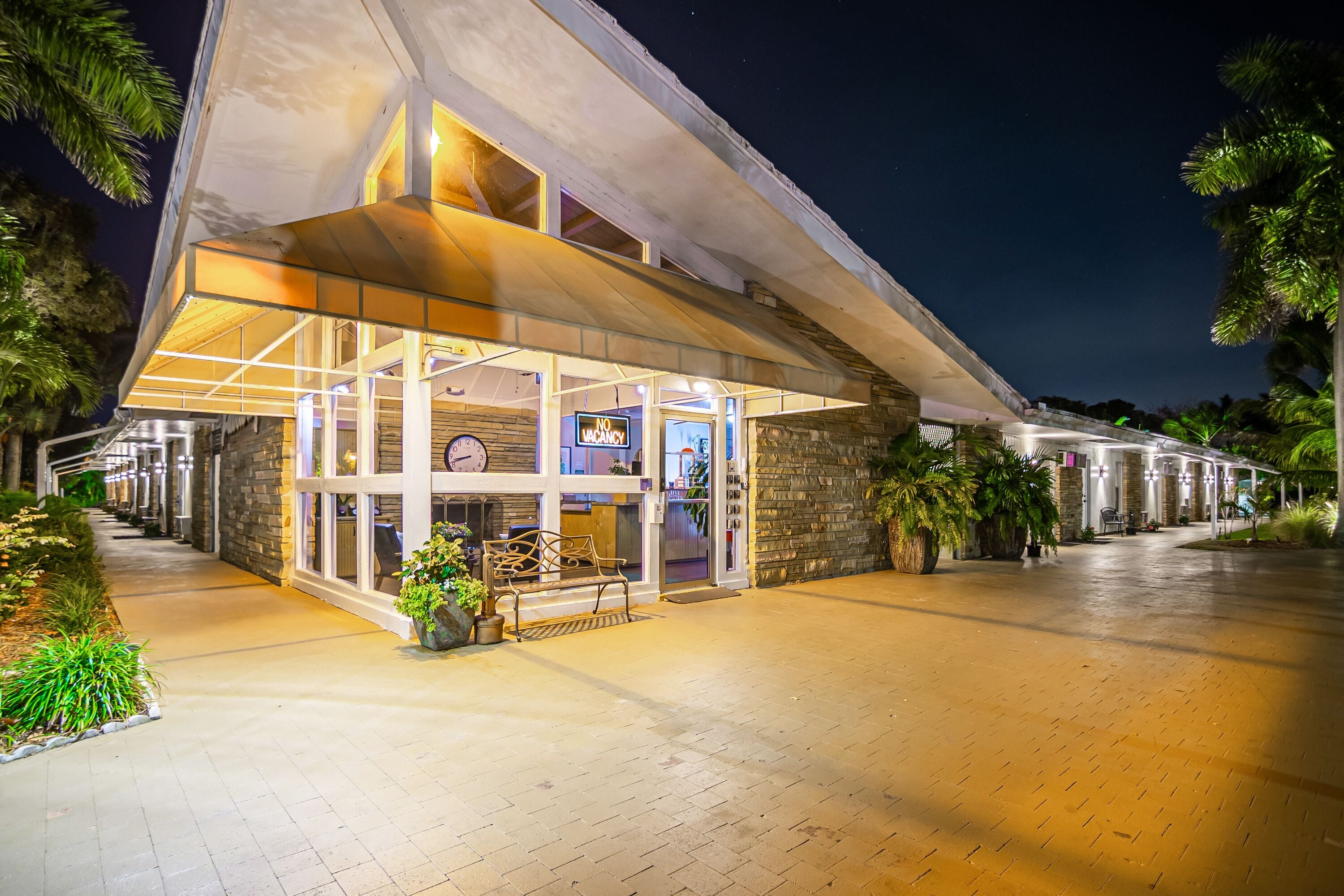A modern hotel entrance with a glass facade, outdoor seating, and a stone wall.