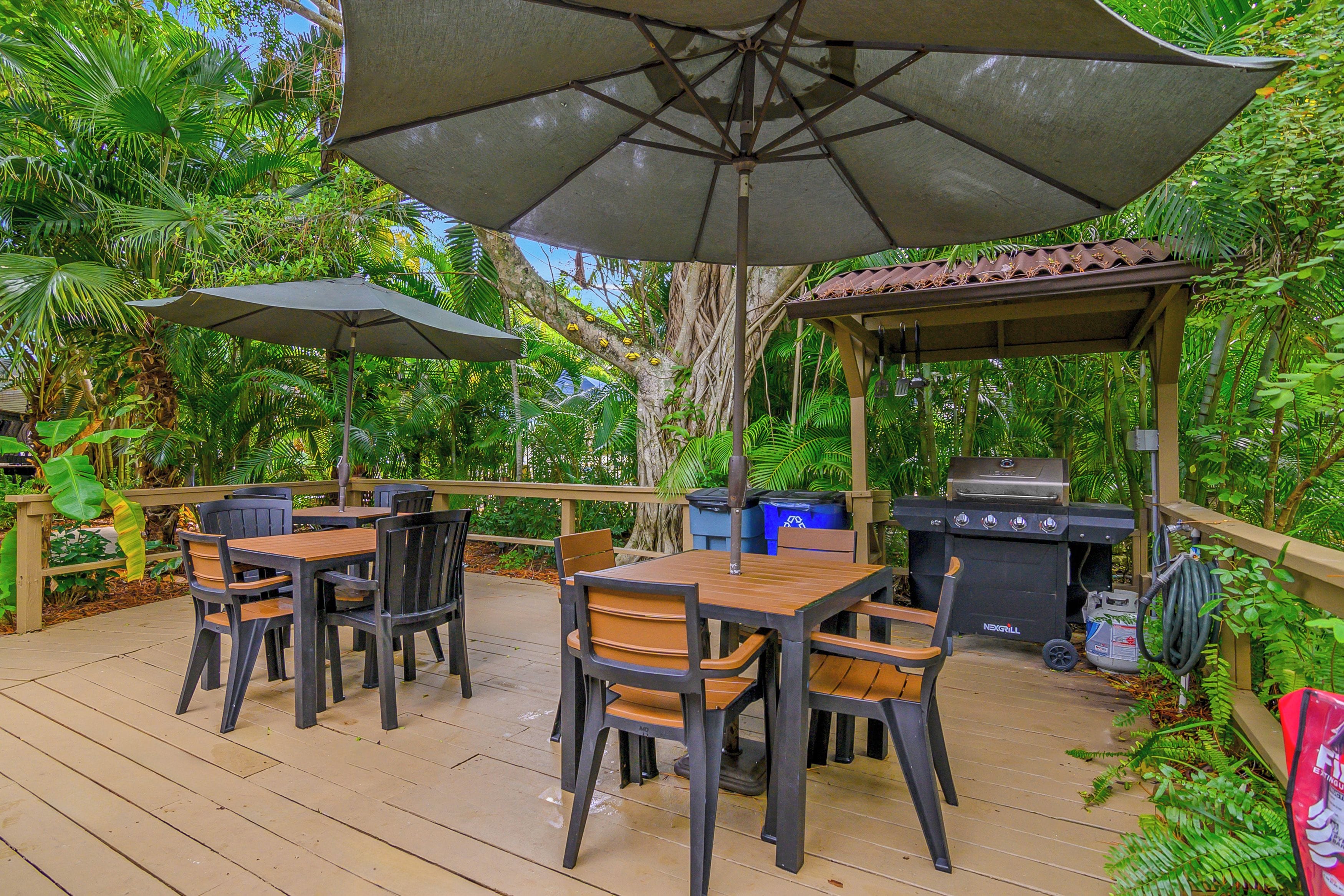 An outdoor patio with a wooden deck, a grill, and a table with chairs.