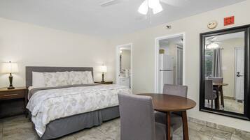 A bedroom with a bed, bedside lamps, a dining table with chairs, a ceiling fan, and a large mirror.
