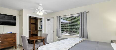 A bedroom with a bed, a desk, a chair, a ceiling fan, a TV, and a window with curtains.