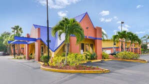 A hotel with a distinctive blue and yellow facade, a parking lot, and surrounding greenery. - Americas Best Value Inn Sarasota Downtown (Sarasota)