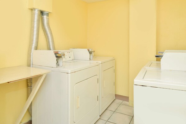 A laundry room with two white washers and dryers, a yellow wall, and a vent on the left. - Americas Best Value Inn Sarasota Downtown (Sarasota)