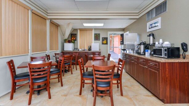 A hotel dining area with wooden tables and chairs, a kitchen counter with appliances, and a view of the adjacent room. - Americas Best Value Inn Sarasota Downtown (Sarasota)
