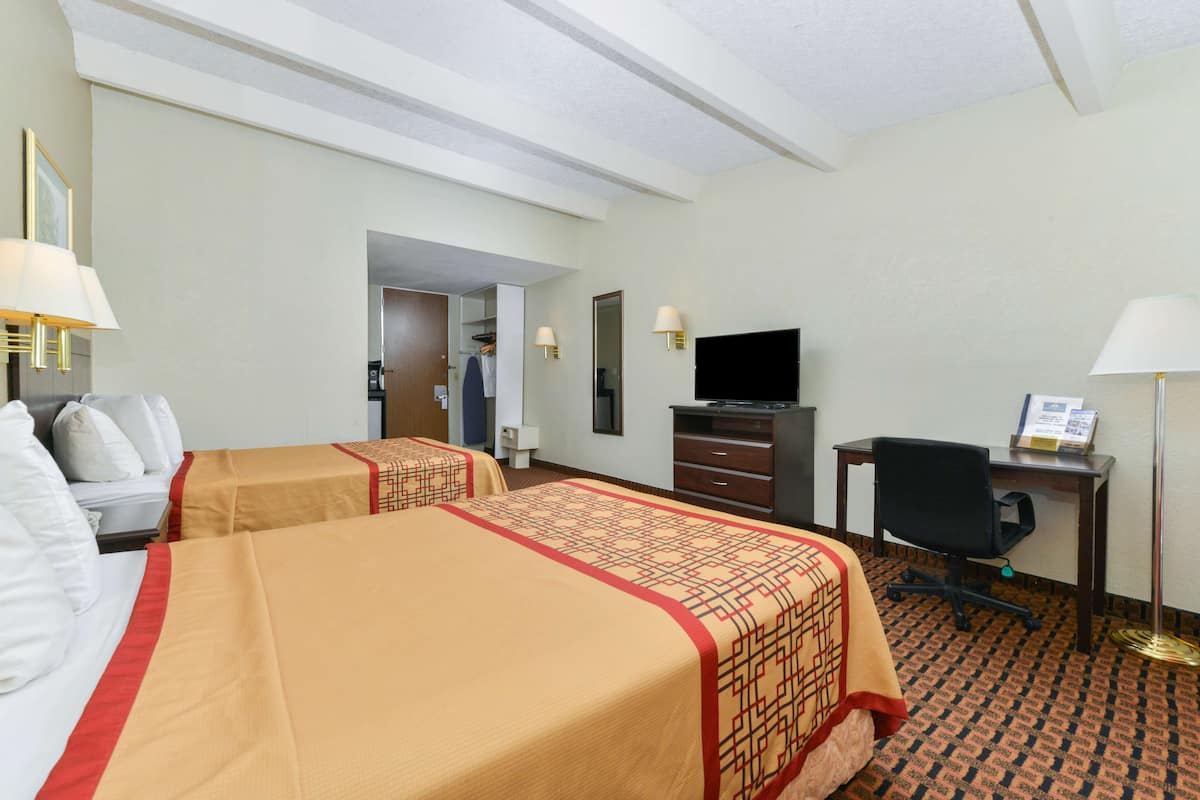 A hotel room with two beds, a desk, a chair, a television, and a wardrobe.