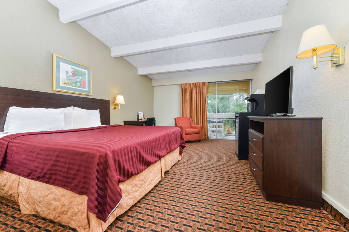 A hotel room with a large bed, a desk with a TV, a chair, a lamp, and a window with curtains.