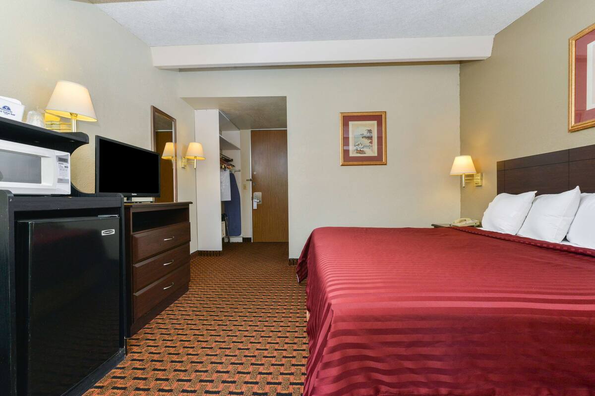 A hotel room with a bed, a TV, a microwave, a dresser, and a door leading to a hallway.
