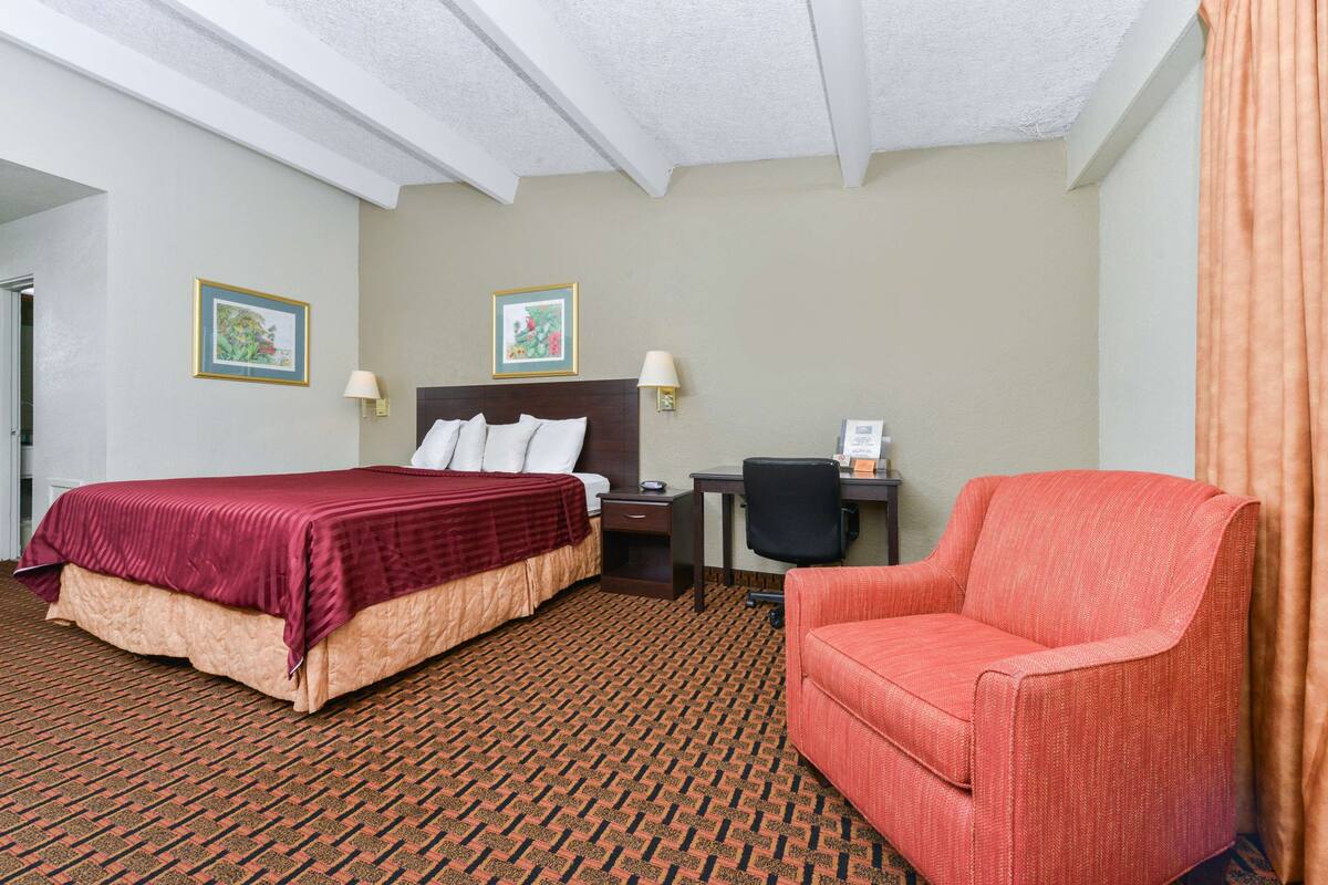 A hotel room with a large bed, a desk, a chair, and two wall-mounted lamps.