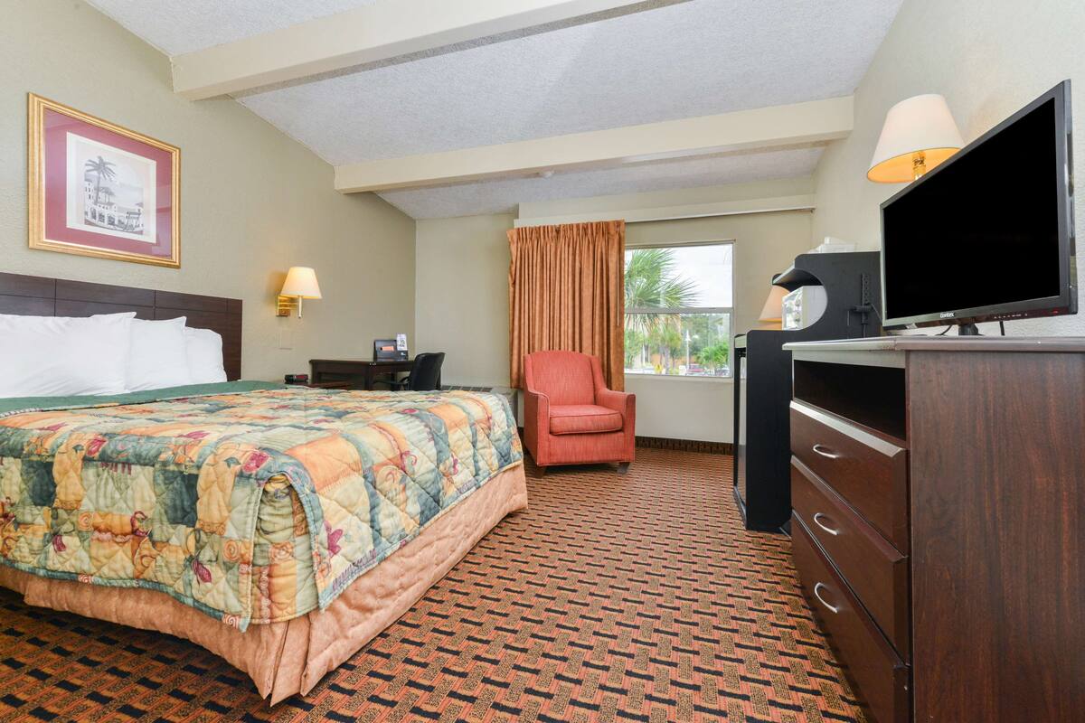 A hotel room with a bed, a desk, a chair, a TV, and a dresser.