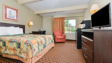 A hotel room with a bed, a desk, a chair, a TV, and a dresser.