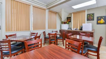 A dining area with wooden tables and chairs, a refrigerator, and a kitchen area with cabinets and a microwave.