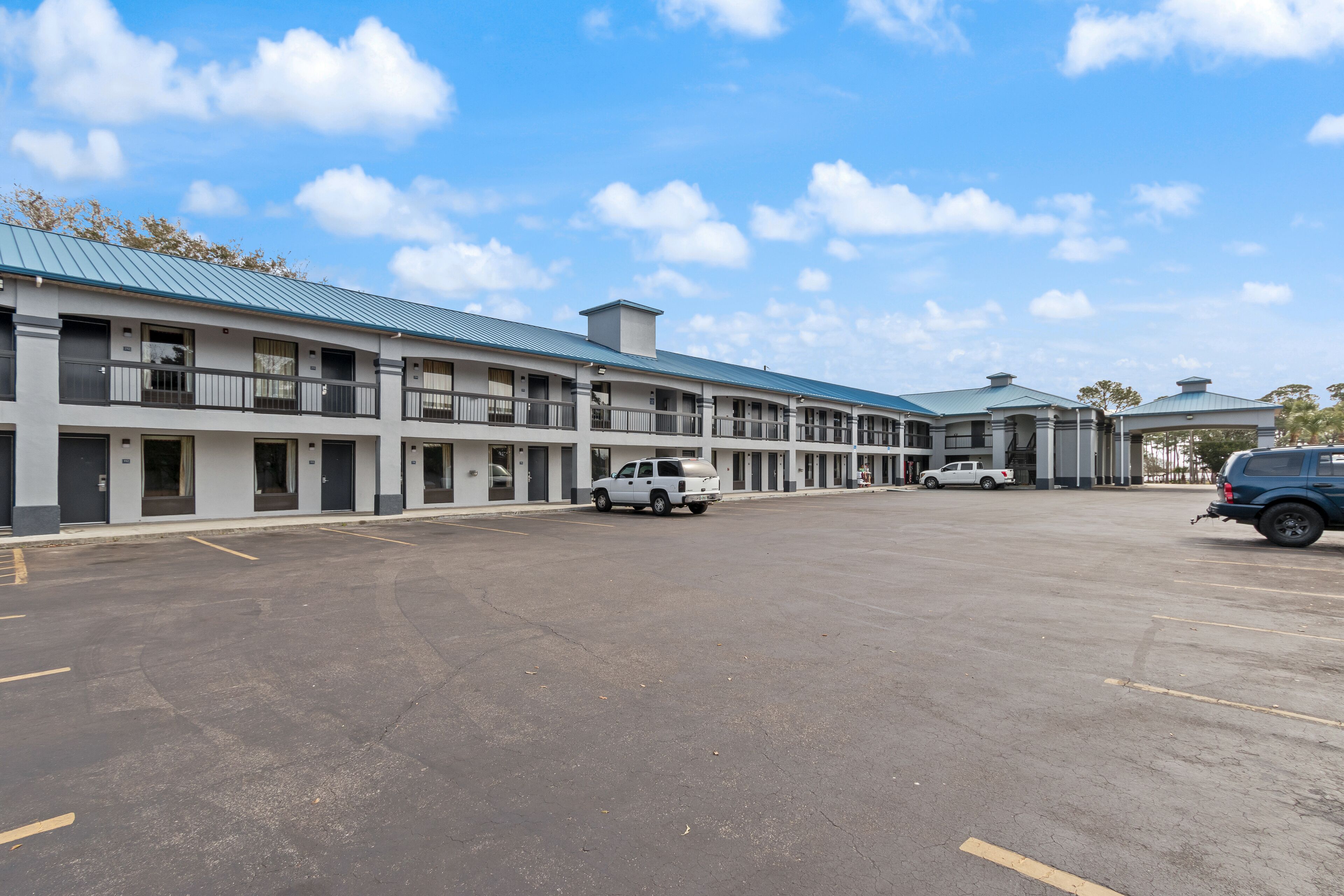 Un motel à plusieurs étages avec un parking, plusieurs véhicules et un ciel dégagé.