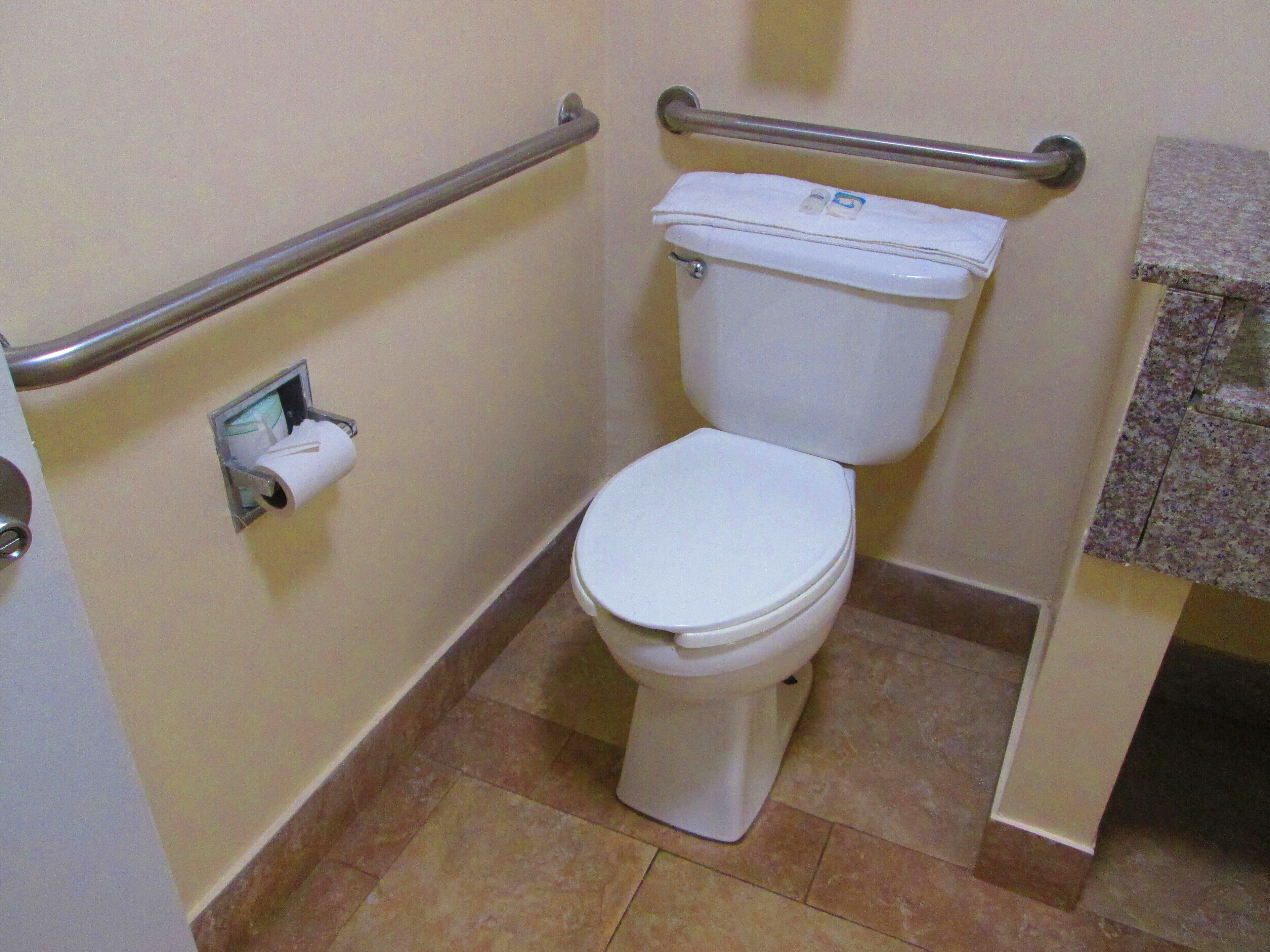 A standard bathroom with a toilet, a handrail, and a paper towel dispenser.